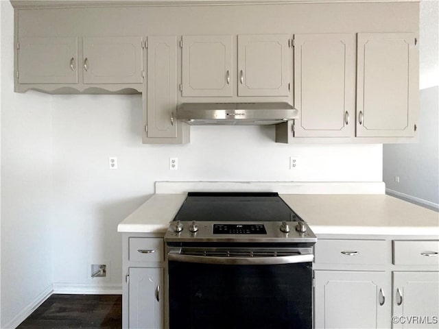 kitchen featuring stainless steel electric stove, under cabinet range hood, light countertops, baseboards, and white cabinetry