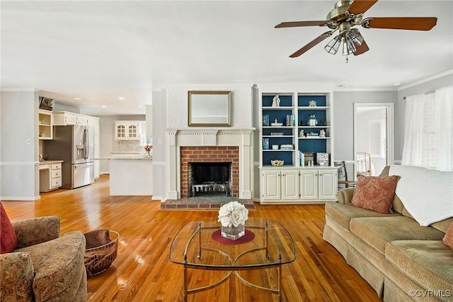 living area featuring ceiling fan, ornamental molding, light wood finished floors, recessed lighting, and a fireplace