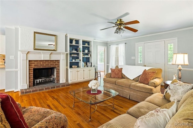 living area featuring ornamental molding, ceiling fan, wood finished floors, and a brick fireplace