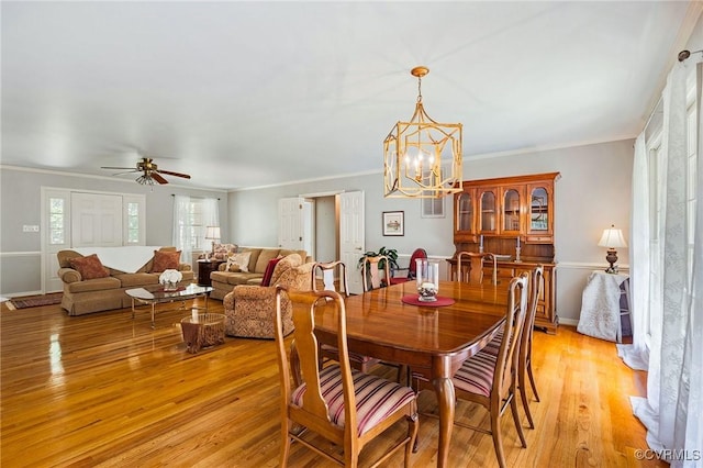 dining area featuring light wood-style floors, a chandelier, crown molding, a ceiling fan, and baseboards