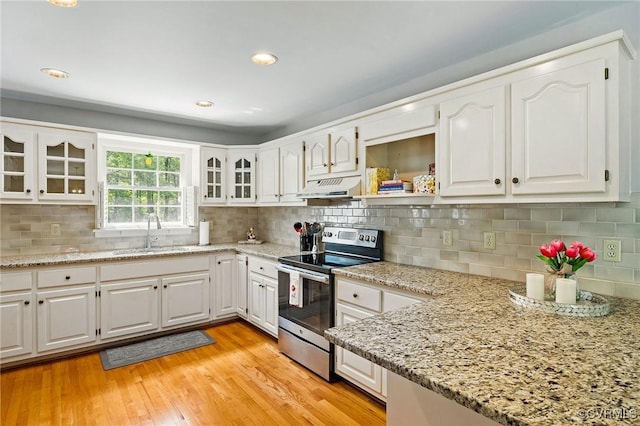 kitchen with stainless steel electric range, a sink, under cabinet range hood, glass insert cabinets, and white cabinets