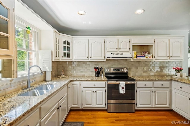 kitchen featuring electric range, under cabinet range hood, a sink, light stone counters, and white cabinetry