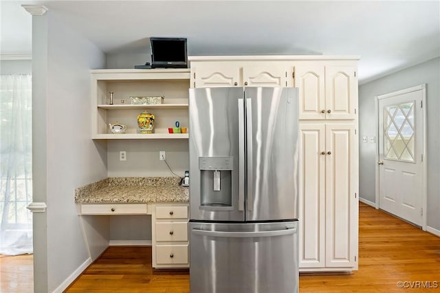 kitchen with stainless steel refrigerator with ice dispenser, light wood-type flooring, light stone counters, white cabinets, and baseboards