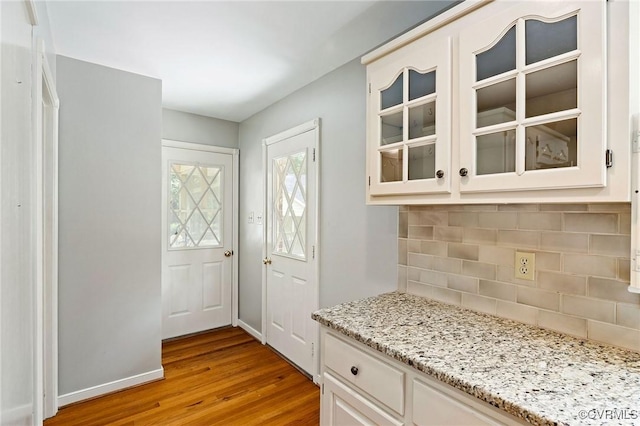 kitchen with wood finished floors, backsplash, glass insert cabinets, light stone countertops, and white cabinetry