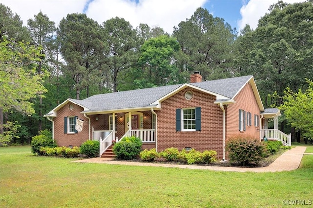 ranch-style home with a porch, brick siding, a front lawn, a chimney, and view of wooded area