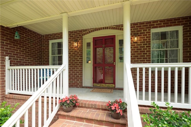 view of exterior entry featuring brick siding and covered porch