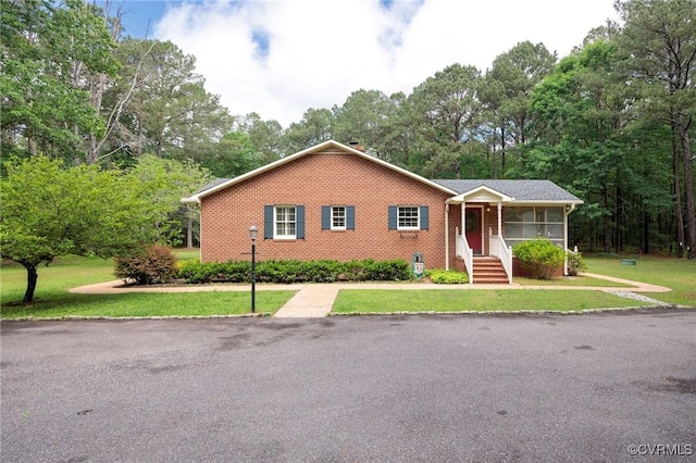 single story home featuring a front lawn, brick siding, and view of scattered trees