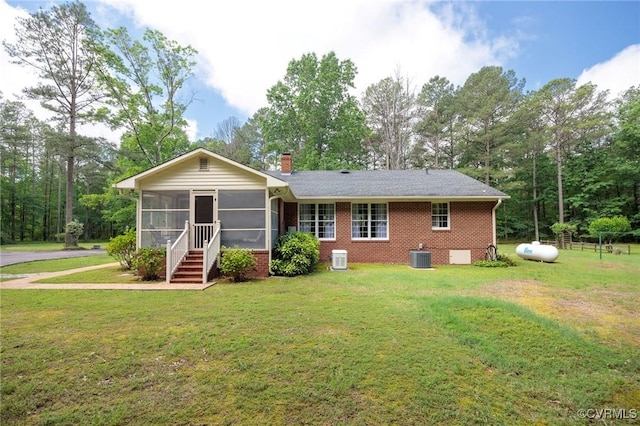 rear view of house featuring a sunroom, brick siding, a chimney, and a yard
