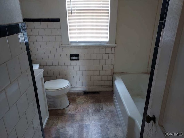 bathroom featuring toilet, tile walls, a tub, and stone finish flooring