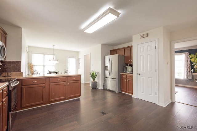 7418 Whirlaway Dr, Midlothian, VA 23112 - kitchen with stainless steel appliances, a peninsula, dark wood-type flooring, brown cabinetry, and decorative light fixtures