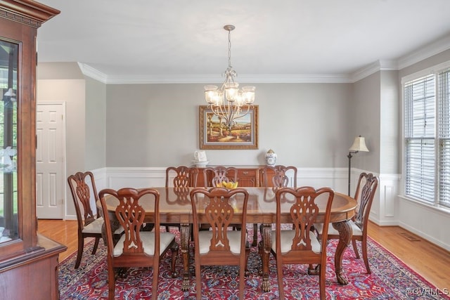 dining area with wood finished floors, a chandelier, healthy amount of natural light, wainscoting, and ornamental molding