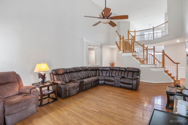 living area with a towering ceiling, a ceiling fan, stairway, light wood-style floors, and baseboards