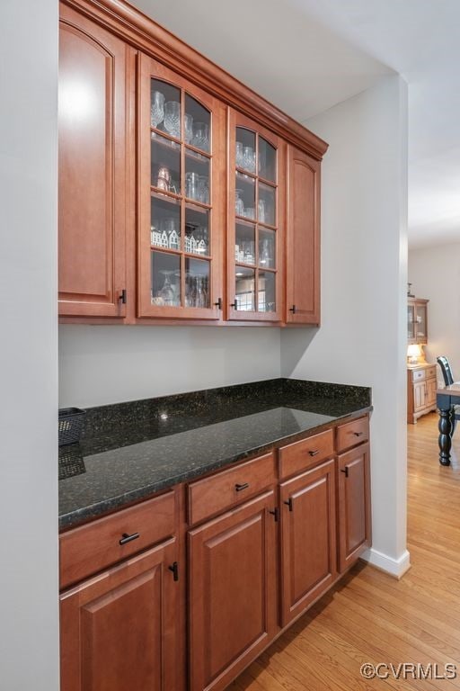 kitchen with light wood finished floors, dark stone counters, brown cabinets, and glass insert cabinets