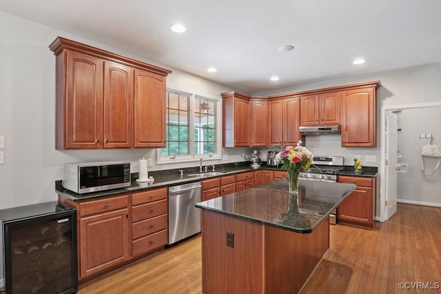 kitchen with appliances with stainless steel finishes, beverage cooler, a sink, under cabinet range hood, and light wood-style floors