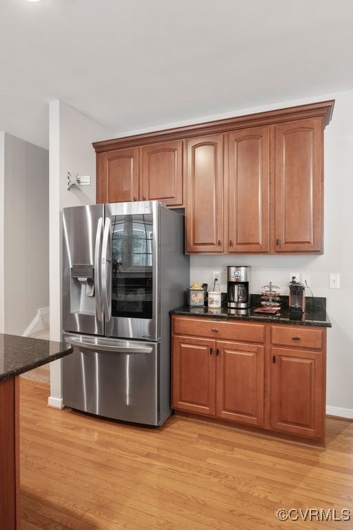 kitchen featuring stainless steel fridge, light wood-style floors, dark stone counters, baseboards, and brown cabinetry