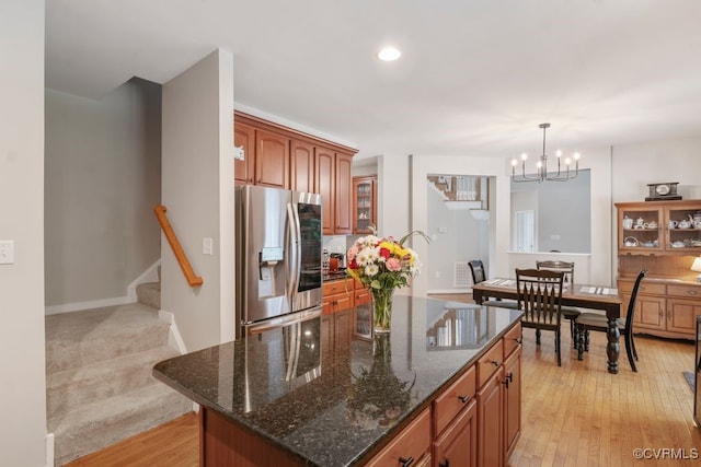 kitchen featuring stainless steel fridge, a chandelier, a kitchen island, dark stone counters, and light wood finished floors