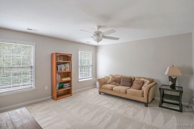 living area featuring baseboards, light colored carpet, a ceiling fan, and plenty of natural light