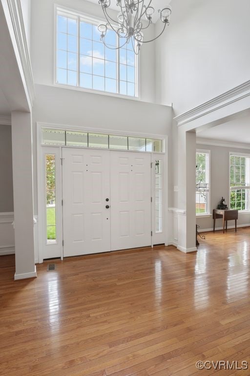 foyer entrance with light wood-type flooring, a chandelier, a towering ceiling, and ornamental molding