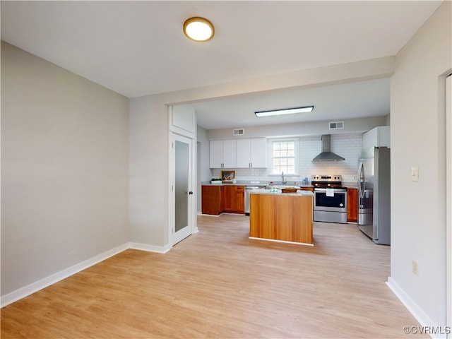 56 Mancha Ave, Claremont, VA 23899 - kitchen featuring stainless steel appliances, wall chimney exhaust hood, light wood finished floors, backsplash, and light countertops