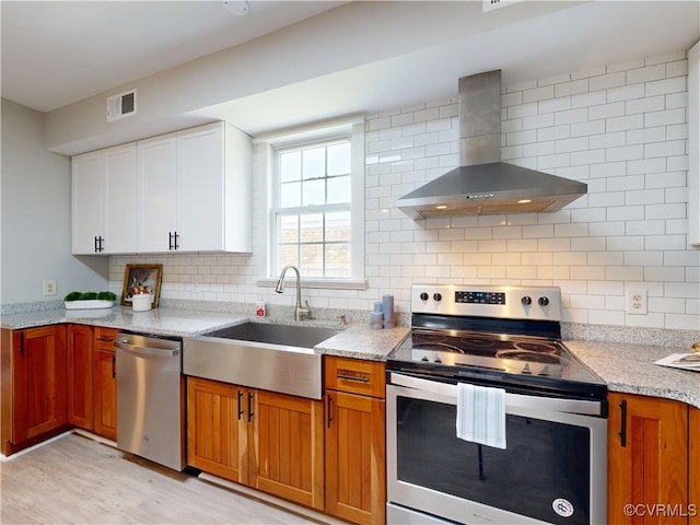 56 Mancha Ave, Claremont, VA 23899 - kitchen with appliances with stainless steel finishes, wall chimney range hood, light stone countertops, decorative backsplash, and light wood-type flooring