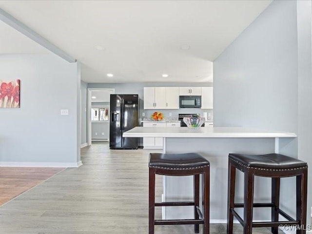 2519 Deerfield Dr, Petersburg, VA 23805 - kitchen featuring black appliances, a breakfast bar, white cabinets, light countertops, and light wood-type flooring