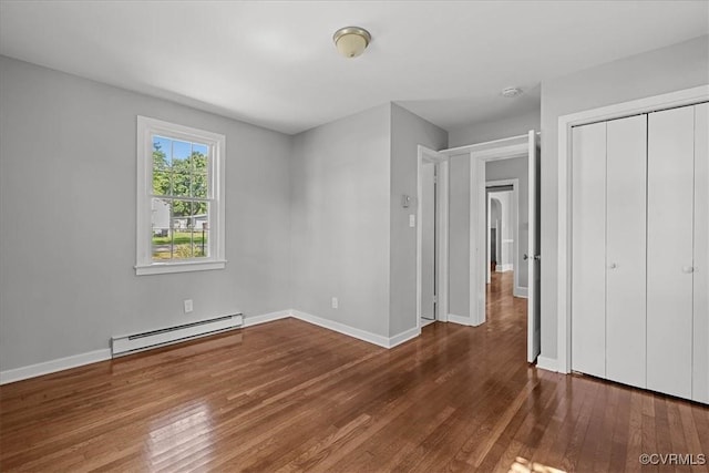 unfurnished bedroom with a baseboard heating unit, wood finished floors, baseboards, and a closet
