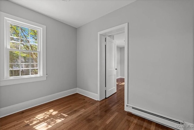empty room featuring a baseboard heating unit, baseboards, and dark wood-type flooring
