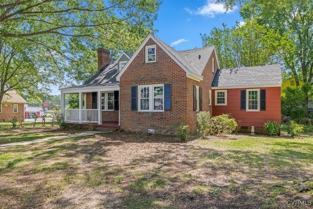 view of front of home featuring a chimney, covered porch, brick siding, and a front yard
