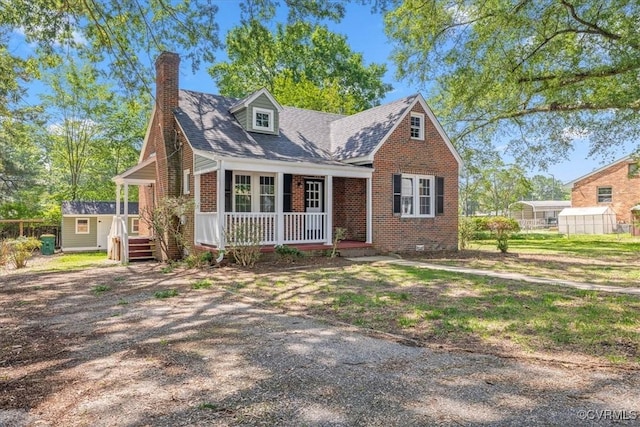 view of front of house with covered porch, brick siding, an outbuilding, a shed, and a chimney