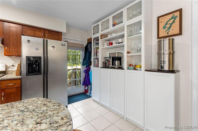 542 Cod Creek Dr, Heathsville, VA 22473 - kitchen with stainless steel fridge with ice dispenser, light stone countertops, brown cabinets, light tile patterned floors, and glass insert cabinets