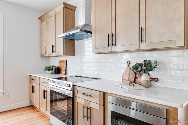 2207 Fairmount Ave, Richmond, VA 23223 - kitchen with wall chimney exhaust hood, stainless steel appliances, tasteful backsplash, light wood-type flooring, and light countertops