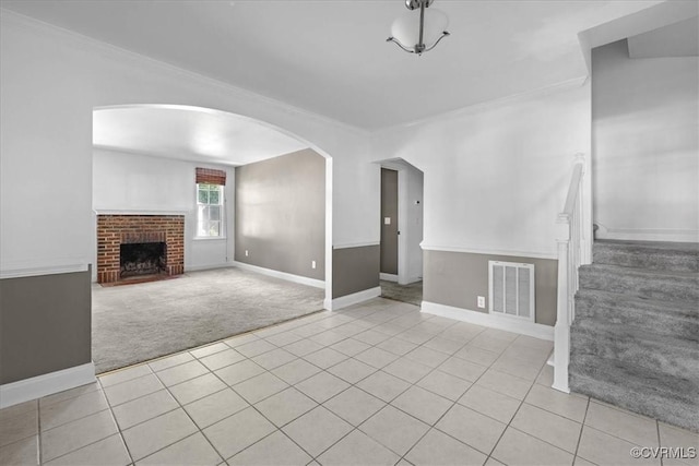 unfurnished living room featuring light colored carpet, arched walkways, light tile patterned floors, baseboards, and crown molding