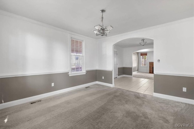 carpeted spare room featuring crown molding, arched walkways, a chandelier, baseboards, and tile patterned flooring