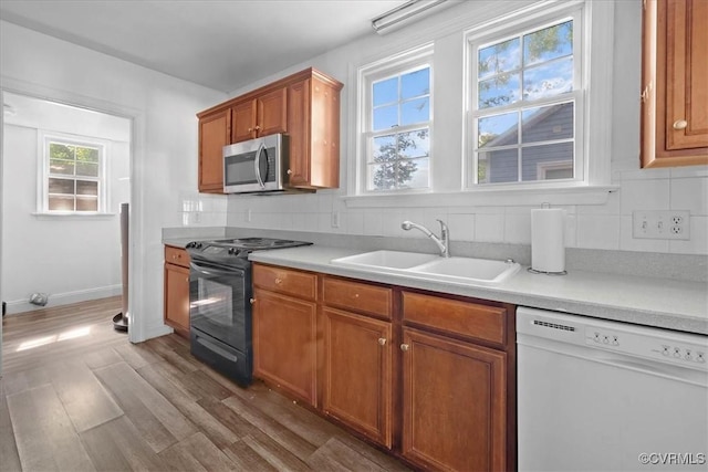 kitchen featuring dishwasher, stainless steel microwave, black range with electric cooktop, a sink, and brown cabinets