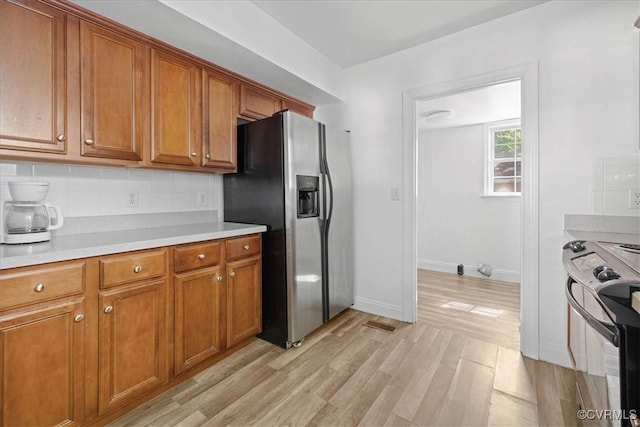 kitchen with black range with electric cooktop, stainless steel refrigerator with ice dispenser, brown cabinetry, and light countertops