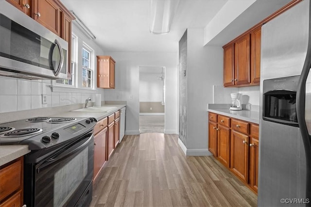 kitchen featuring stainless steel appliances, a sink, light wood-style floors, light countertops, and decorative backsplash