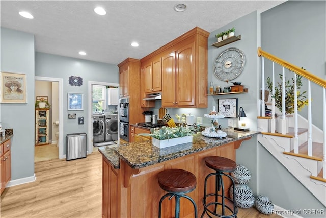 6304 Belroi Rd, Abingdon, VA 23061 - kitchen featuring independent washer and dryer, appliances with stainless steel finishes, dark stone counters, under cabinet range hood, and light wood-style flooring