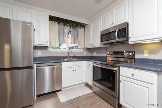 kitchen with appliances with stainless steel finishes, a sink, dark countertops, and white cabinetry