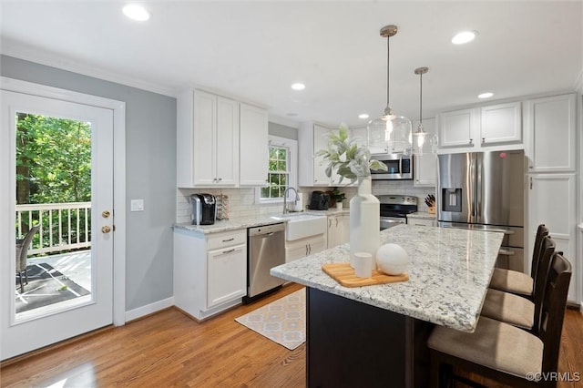 kitchen with appliances with stainless steel finishes, a sink, a kitchen breakfast bar, white cabinetry, and backsplash