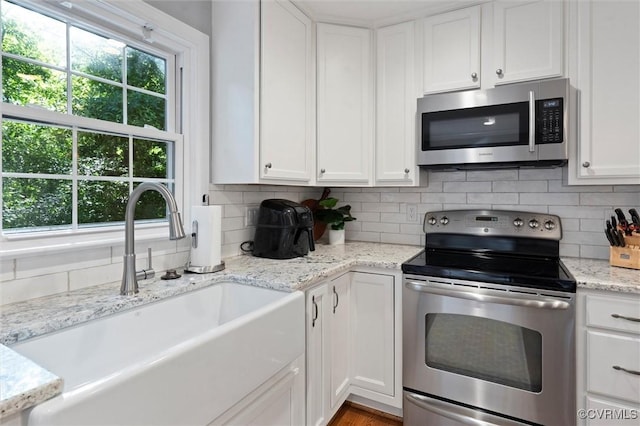 kitchen featuring stainless steel appliances, a sink, white cabinets, tasteful backsplash, and light stone counters