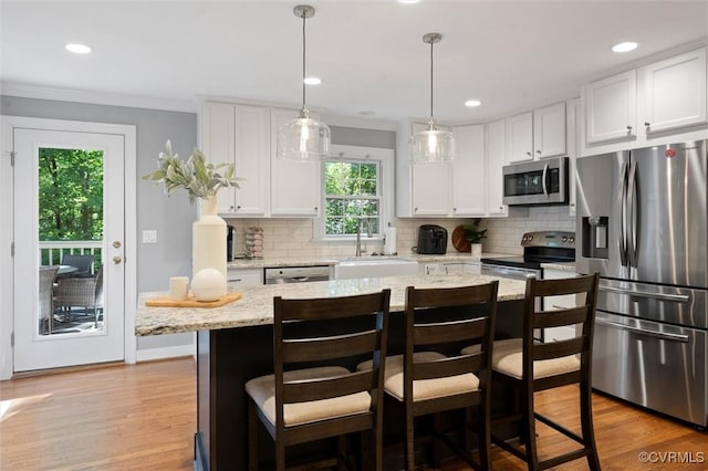 kitchen with stainless steel appliances, white cabinets, light wood-type flooring, tasteful backsplash, and ornamental molding