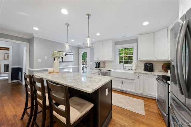 kitchen featuring stainless steel appliances, a sink, ornamental molding, white cabinetry, and backsplash