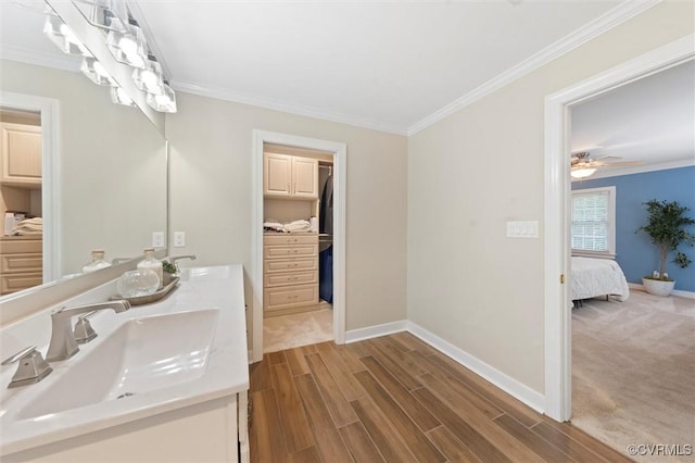 bathroom featuring baseboards, crown molding, wood finished floors, double vanity, and ensuite bath