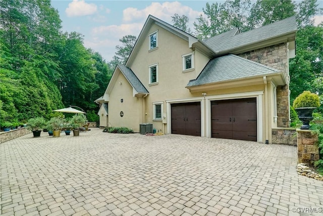 717 Old Stream Rd, Manakin Sabot, VA 23103 - view of side of home featuring stucco siding, a garage, stone siding, decorative driveway, and central AC