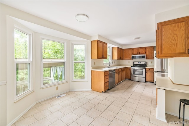 9645 Benbow Rd, North Chesterfield, VA 23235 - kitchen with stainless steel appliances, a sink, light countertops, brown cabinetry, and light tile patterned flooring