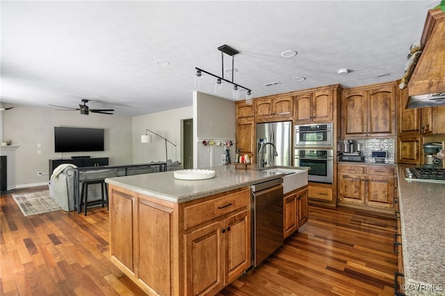 160 Woodland Trl, West Point, VA 23181 - kitchen featuring appliances with stainless steel finishes, dark wood-style floors, a ceiling fan, a kitchen island with sink, and brown cabinets
