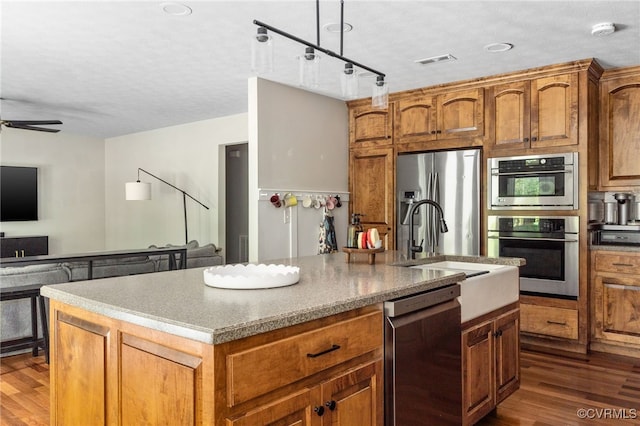 160 Woodland Trl, West Point, VA 23181 - kitchen with appliances with stainless steel finishes, a center island with sink, dark wood-style floors, a sink, and brown cabinets