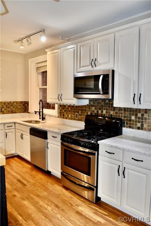 2923 Monument Ave Unit 1, Richmond, VA 23221 - kitchen with stainless steel appliances, a sink, white cabinetry, decorative backsplash, and light stone counters