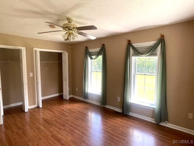 22290 Butterwood Rd, Dinwiddie, VA 23803 - unfurnished bedroom featuring dark wood-style flooring, baseboards, multiple closets, a ceiling fan, and a textured ceiling
