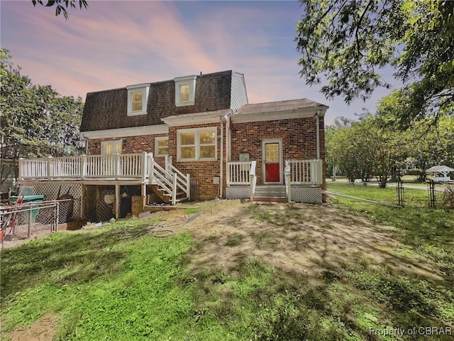 402 N Ivy Ave, Highland Springs, VA 23075 - back of house at dusk featuring mansard roof, brick siding, a wooden deck, and a shingled roof